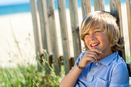 Portrait of cute boy relaxing nect to wooden fence on beach.の写真素材