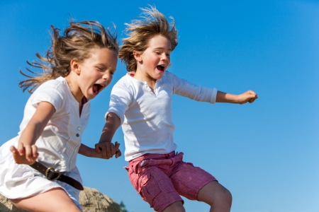 Two kids shouting and jumping together outdoors.の写真素材