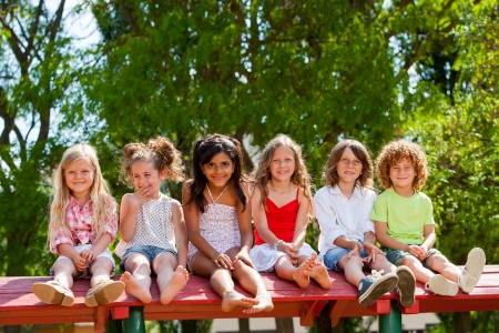 Portrait of happy children sitting together wooden structure in park.の写真素材