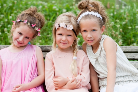Portrait of three cute girl friends on wooden bench in park. の写真素材