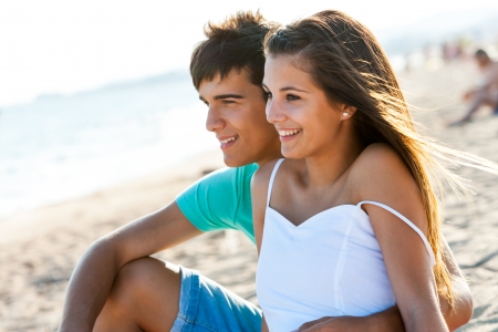 Cute teen couple sitting together on beach at sunset.の写真素材