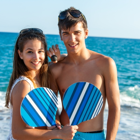 Portrait of cute teen couple holding beach tennis rackets.の写真素材