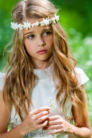 Close up portrait of cute girl in white dress holding flower outdoors.