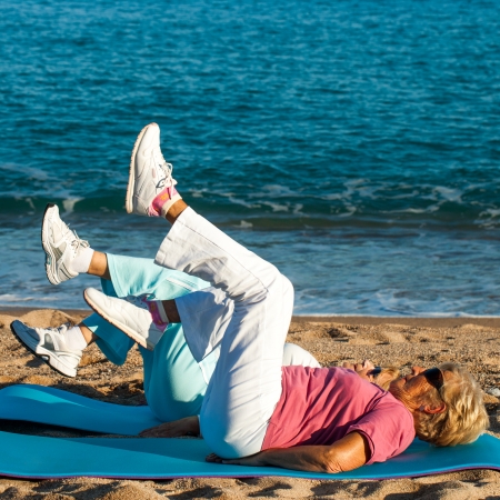 Two elderly women exercising legs toghether on beach.の写真素材