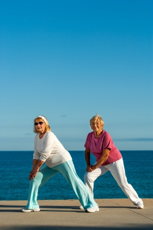Two golden age women stretching legs at seafront.の写真素材