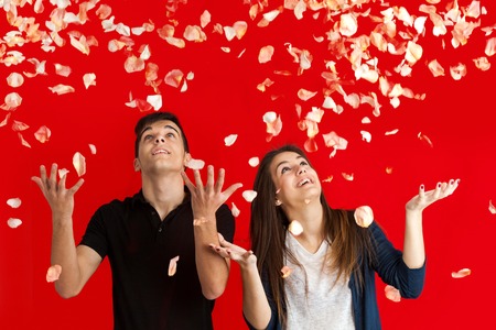 Couple with arms raised having fun throwing rose petals over red background.の写真素材
