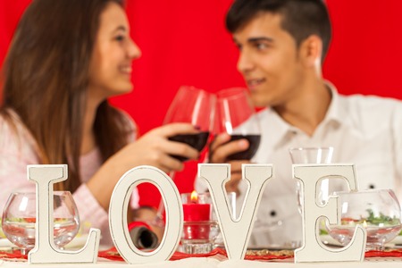 Close up of love block letters on romantic dinner table with couple making toast in background.の写真素材