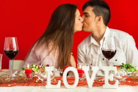 Close up of romantic dinner table with kissing young couple in background.の写真素材
