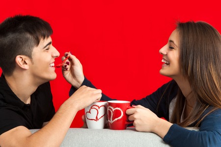 Close up portrait of teen couple having great time drinking coffee.Isolated on red background.の写真素材