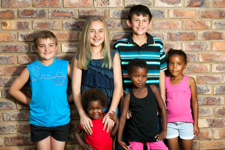 Multiracial group of kids standing together against brick wall outdoors.の写真素材