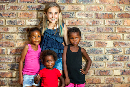 Portrait of cute girl standing with african friends against brick wall.の写真素材