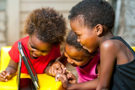 Close up portrait of three african young girls playing together on digital tablet.の写真素材