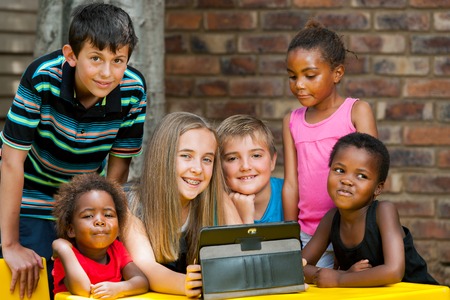 Group of diverse kids playing together on digital tablet outdoors.の写真素材