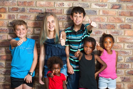 Diversity portrait of kids against brick wall doing thumbs up.の写真素材