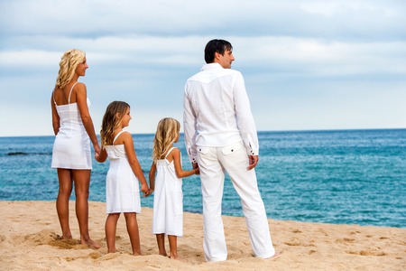 Cute family in white on beach looking into the distance.の写真素材
