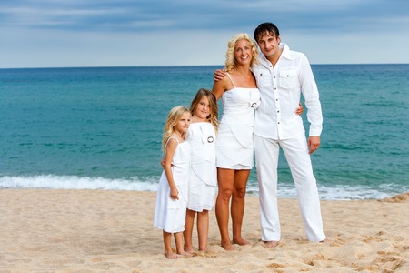 Full length portrait of cute family dressed in white on beach.の写真素材