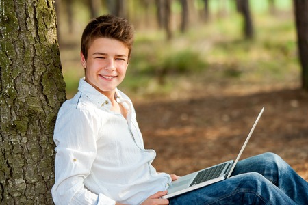 Close up portrait of teen boy in park with laptop.の写真素材