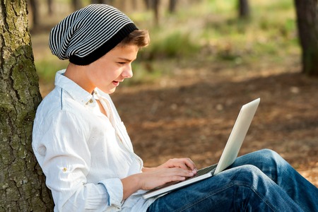 Portrait of teen boy chatting on laptop in park.の写真素材