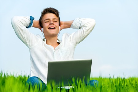Close up portrait of teen in green grass field listening to music with eyes closed.の写真素材