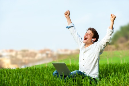 Happy teen with laptop in green field shouting of joy.の写真素材