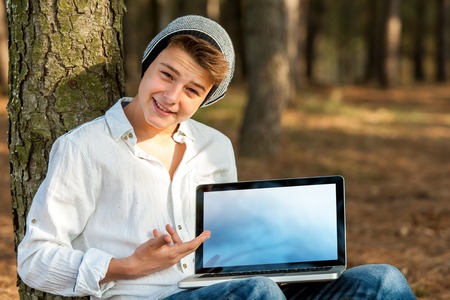 Portrait of handsome teen student pointing at blank laptop screen with hand.の写真素材