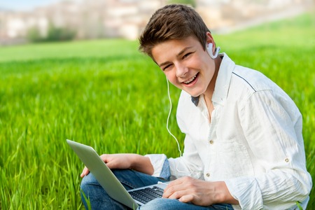 Portrait of handsome teen student working on laptop in green grass field.の写真素材