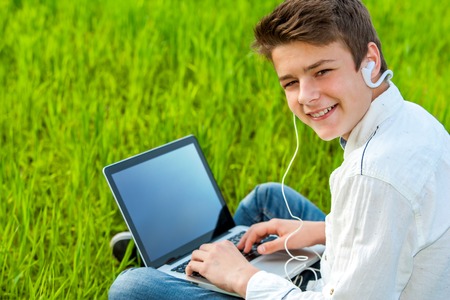 Close up portrait of teen student working on laptop in green grass field.の写真素材