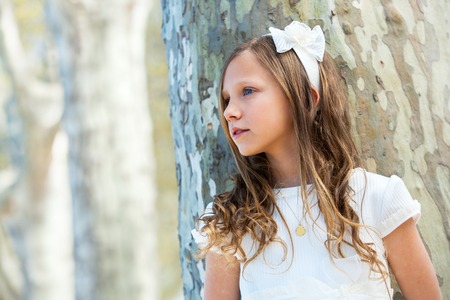 Portrait of young girl in white dress standing next to tree.の写真素材