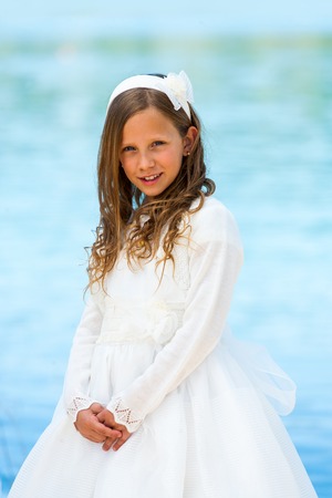 Portrait of cute girl in communion dress with water background.の写真素材