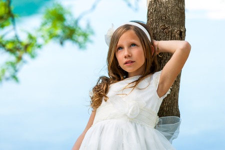 Close up portrait of cute girl in white dress against tree.の写真素材