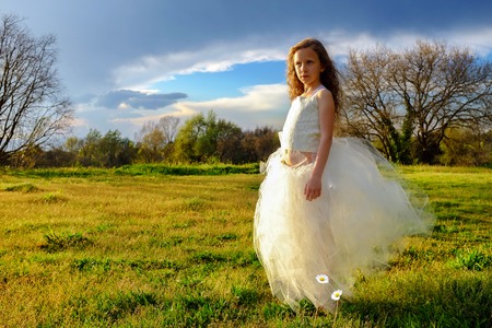 Full length Portrait of cute girl wearing white dress in grass field at sunset. の写真素材