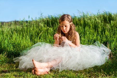 Young girl wearing white dress relaxing in green meadow.の写真素材