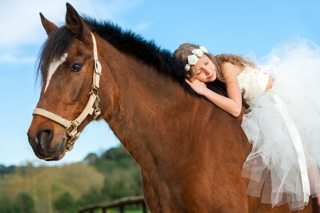Portrait of young girl in white dress sleeping on horseback.の写真素材