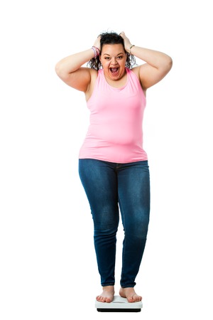 Portrait of overweight teen sanding on diet scale with shocking face expression.の写真素材