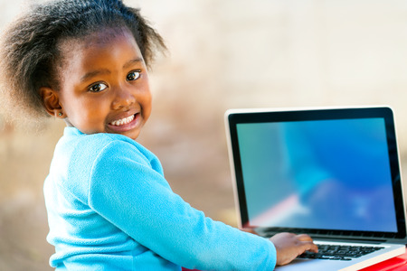 Cute African student working on laptop showing blank screen with copy space.
