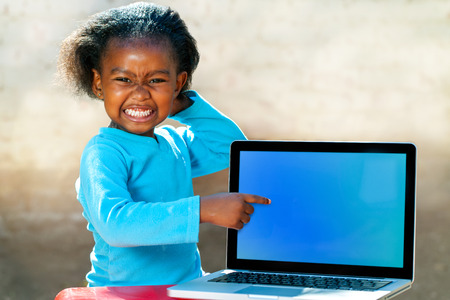 Portrait of African girl with funny face expression pointing at blank laptop screen.の写真素材