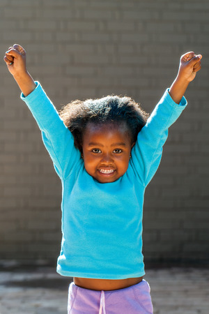 Portrait of little African girl raising arms outdoors.の写真素材