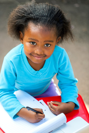 Portrait of small African kid writing in notebook at desk.の写真素材
