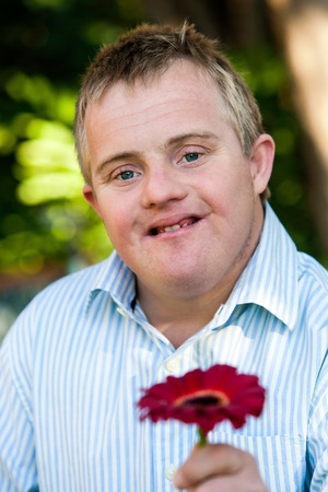 Close up outdoor portrait of handsome boy with down syndrome holding red flower.の写真素材