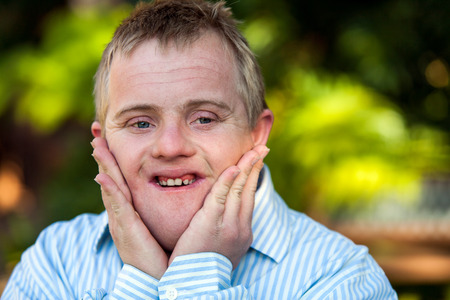 Close up portrait of handicapped boy with hands on face outdoors.の写真素材