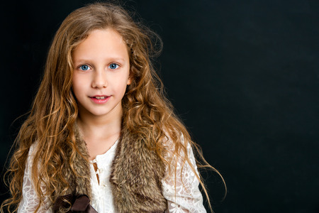 Close up portrait of young girl with long curly hair against dark background.の写真素材