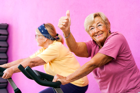 Portrait of happy Senior fitness woman doing thumbs up at spinning session in gym.の写真素材