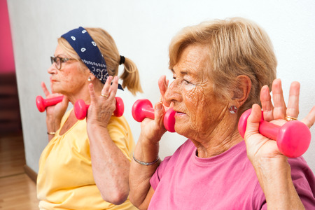 Close up portrait of two senior women doing exercise with weights in health club.の写真素材