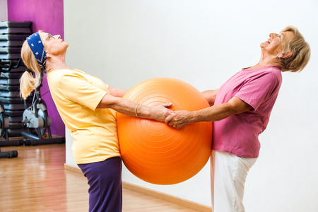 Portrait of two Elderly women stretching muscles together with fitness ball in gym.の写真素材