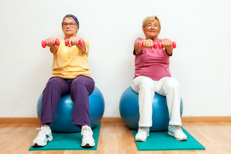 Portrait of Two elderly women doing muscle exercises with weights in gym.の写真素材