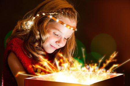 Close up Conceptual portrait of cute girl staring at gift box with lights rays.の写真素材