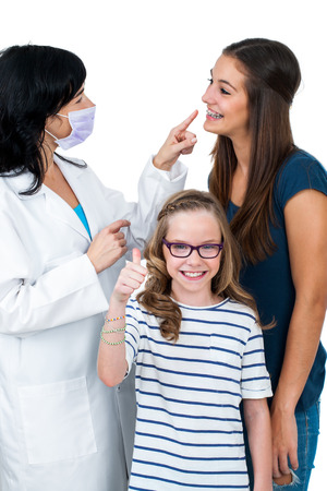 Little girl doing thumbs up sign together with older sister ready for dental check up.Isolated on white background.の写真素材