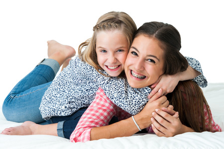 Close up portrait of young girl embracing older teen sister on bed.の写真素材