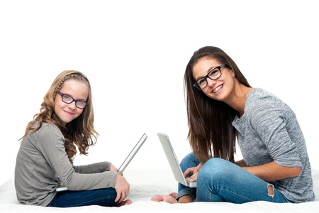 Portrait of teen student with younger sister working on laptops.Isolated on white background.の写真素材