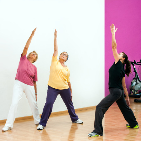 Female fitness coach doing aerobic workout with Senior women in health club.の写真素材